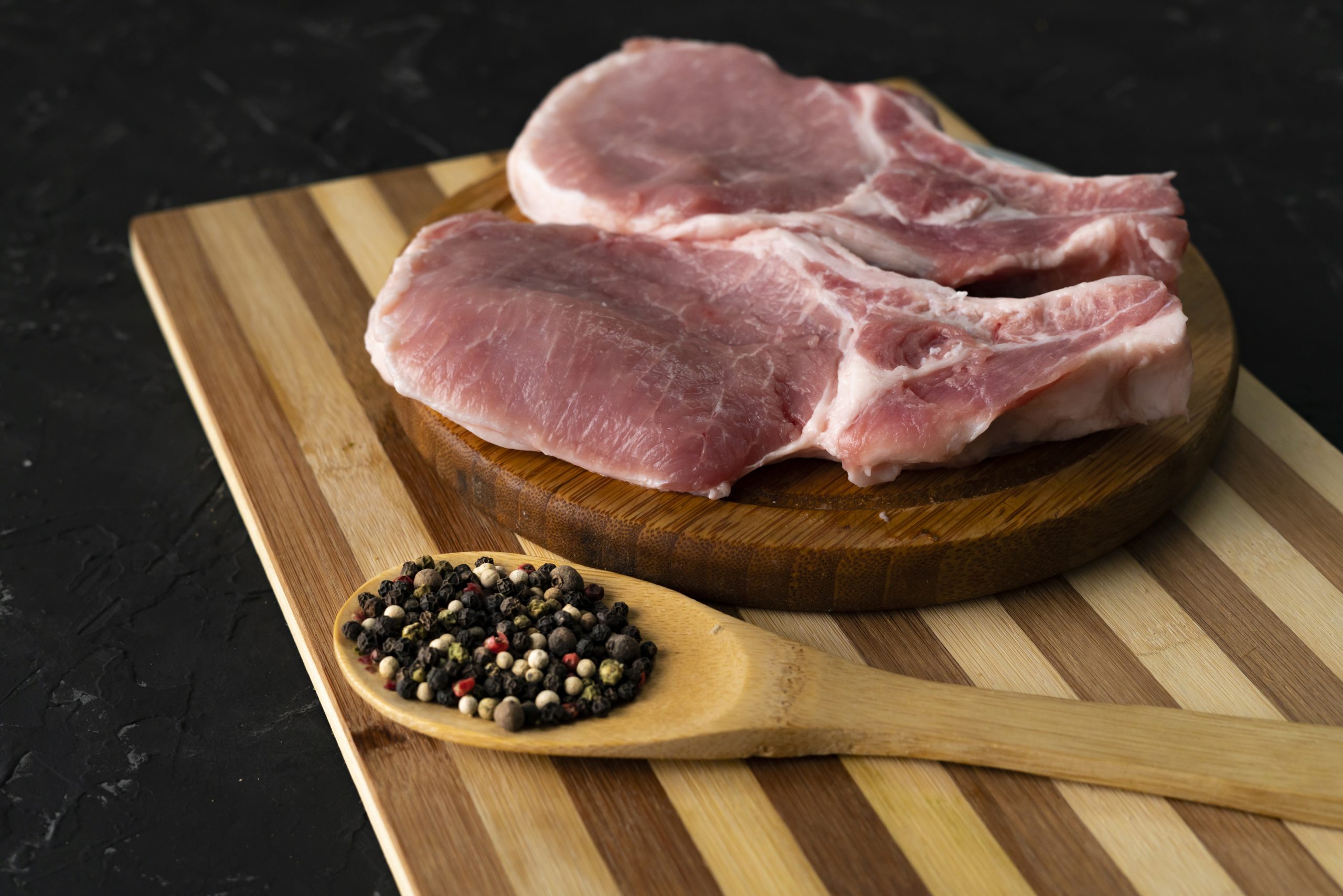 raw pork fillet on a slicing board, wooden spoon with spices and pepper, fat junk food, uncooked raw pork fillet on a slicing board, wooden spoon with spices and pepper, fat junk food, uncooked